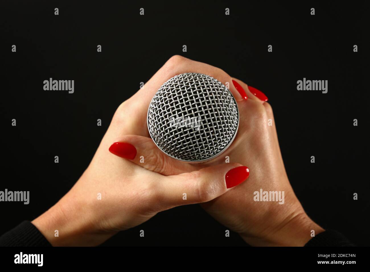 Cropped Hands Of Woman Holding Microphone Over Black Background Stock Photo