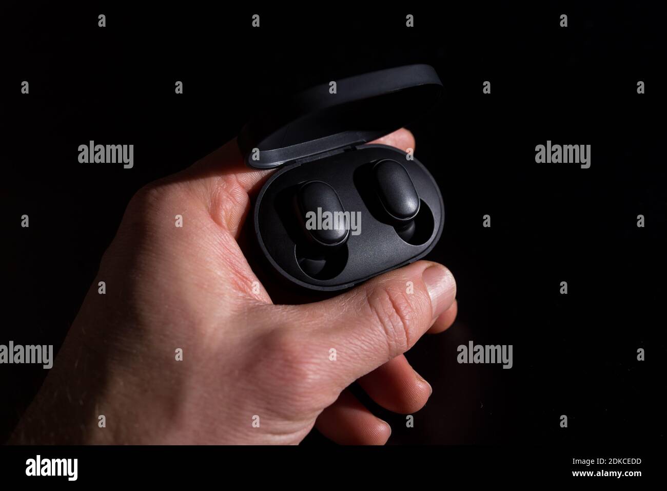Black wireless headphones in hand, isolated on black background. Stock Photo