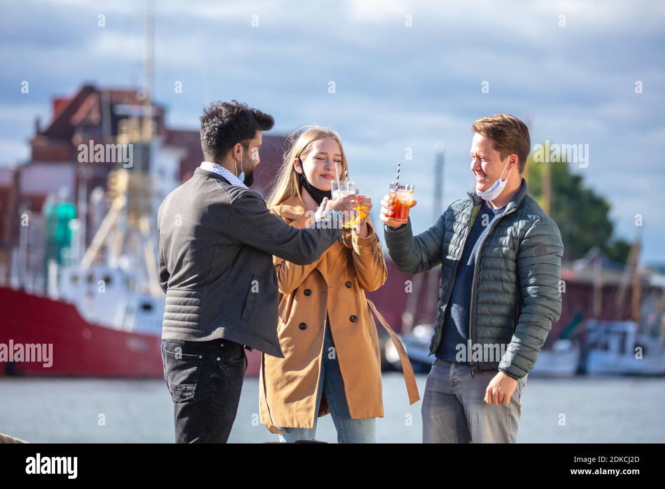 Two men and a woman with everyday masks in Corona time, out and about in the city in the cold season, drinks outdoors, small meeting among acquaintances, Stock Photo