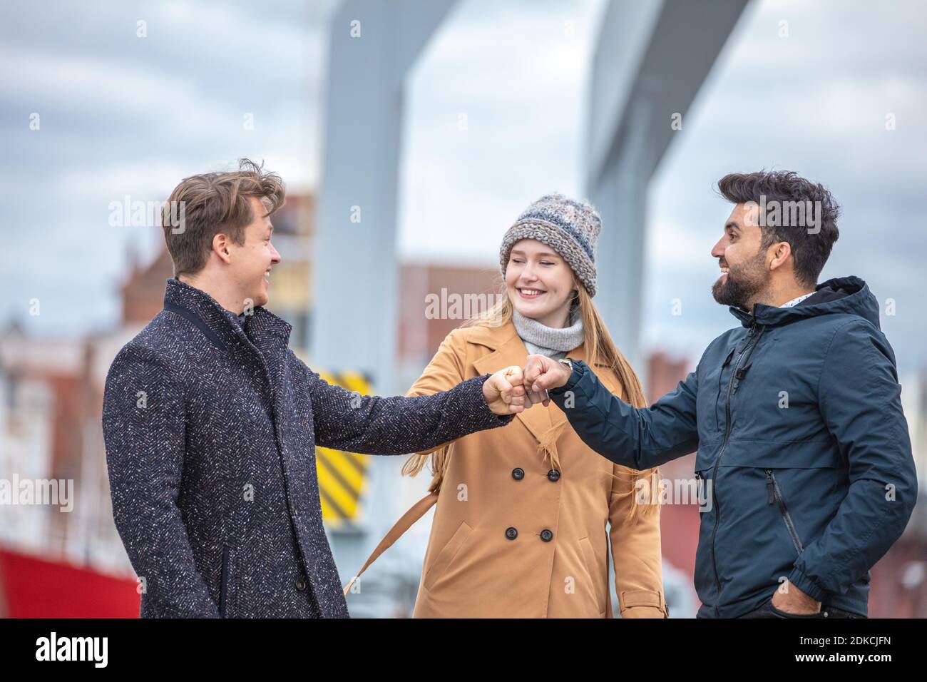 Two men and a woman greeting at Corona time, without everyday masks, out and about in the city in the cold season, Stock Photo