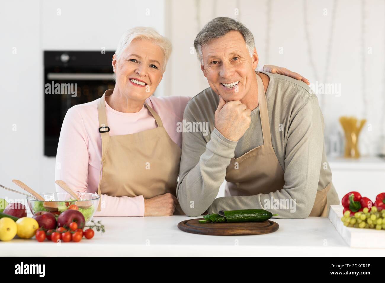 Happy Senior Couple Posing In Kitchen, Hugging Cooking Dinner Together Stock Photo