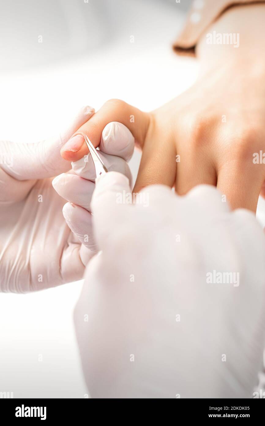 Manicure master is removing cuticles with a nail scissors in a nail