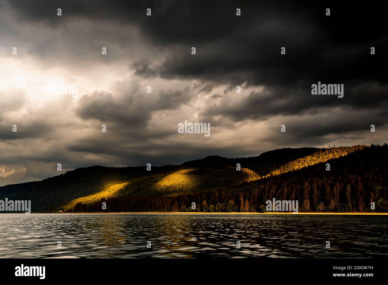 Storm clouds and light mood over Altlach, on the Walchensee in the Bavarian Alps, the Karwendel and Ester Mountains. Intense sunlight illuminates sections of the forest while dark storm clouds shade the rest. Stock Photo