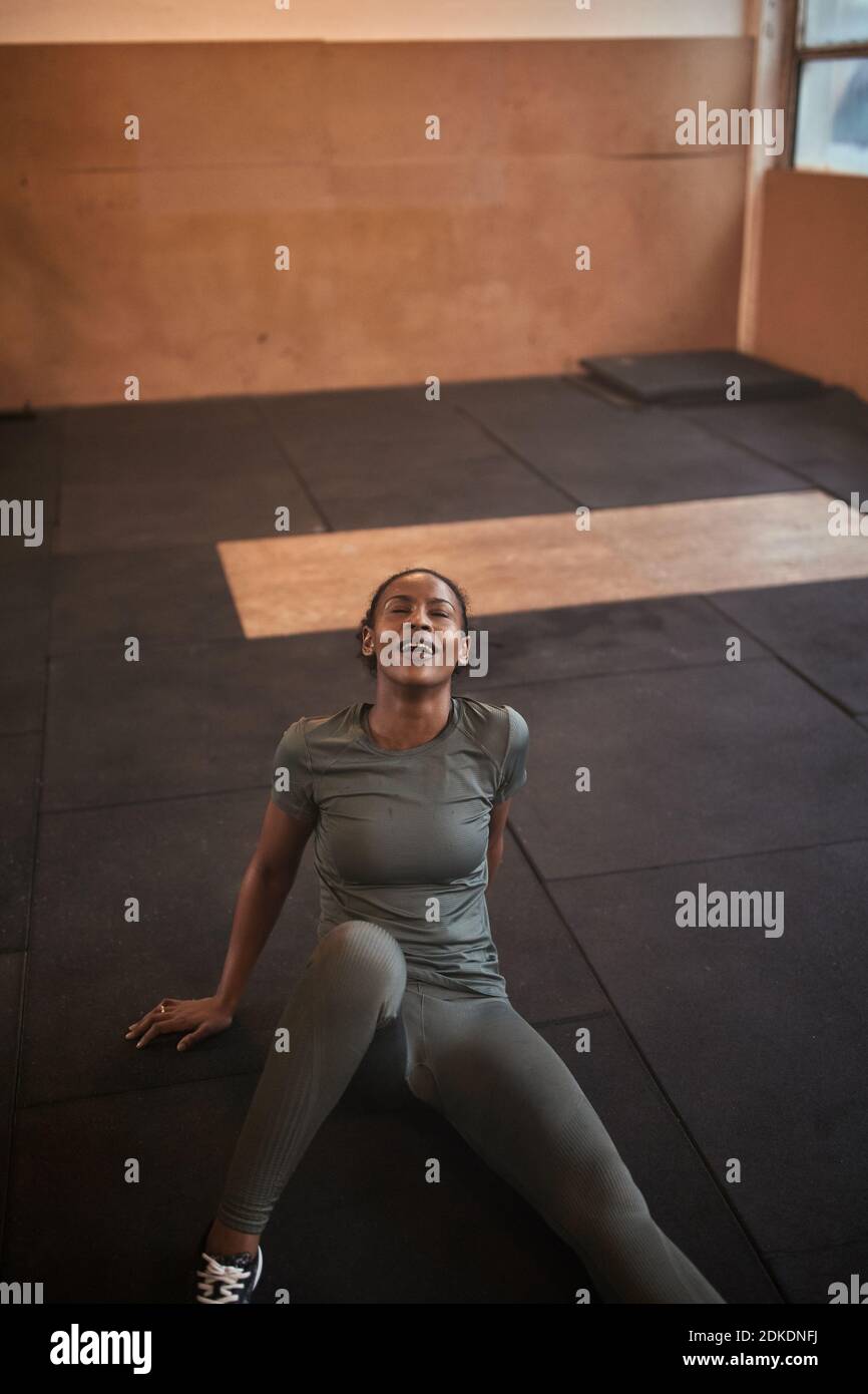 Fit young African American woman in sportswear sitting on a gym floor and sweating after a workout Stock Photo