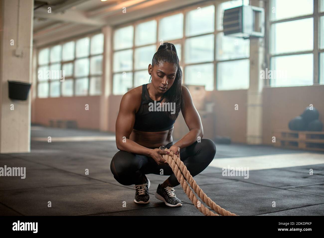 Fit young Indian woman in sportswear crouching on a gym floor and looking exhausted after a workout with battle ropes Stock Photo Alamy