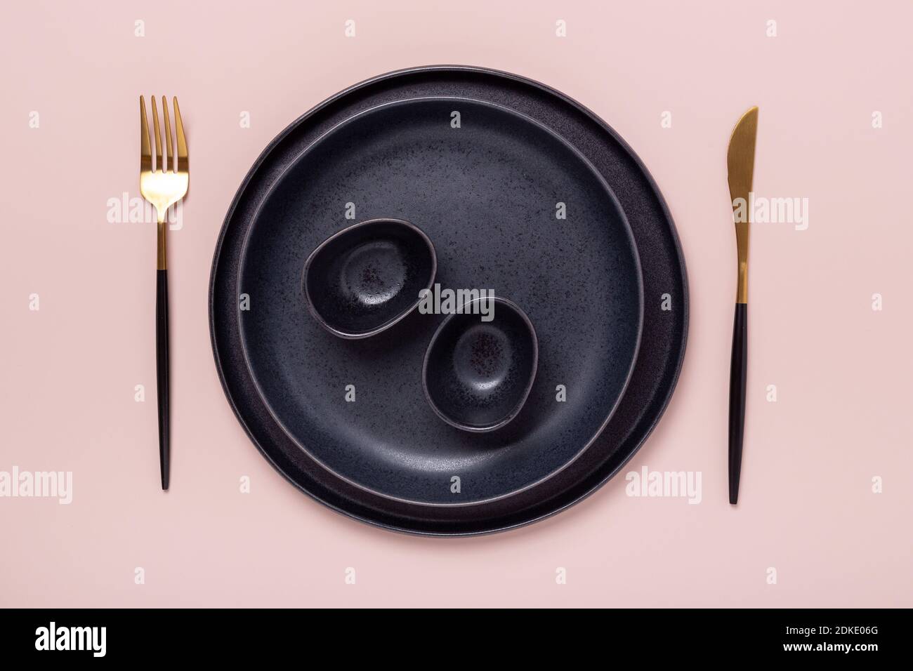 Set of black ceramic plates and cutlery on pastel pink background. Copy ...