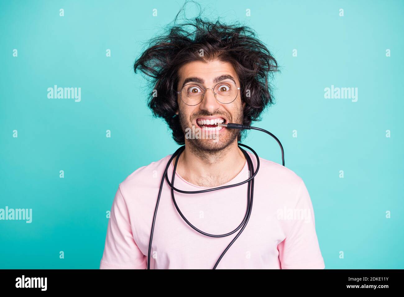 Close up portrait of weird hairdo crazy person biting tooth cable isolated on turquoise color background Stock Photo