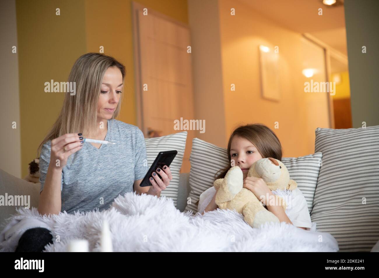 Mother check child temperature and holds phone to call the doctor Stock