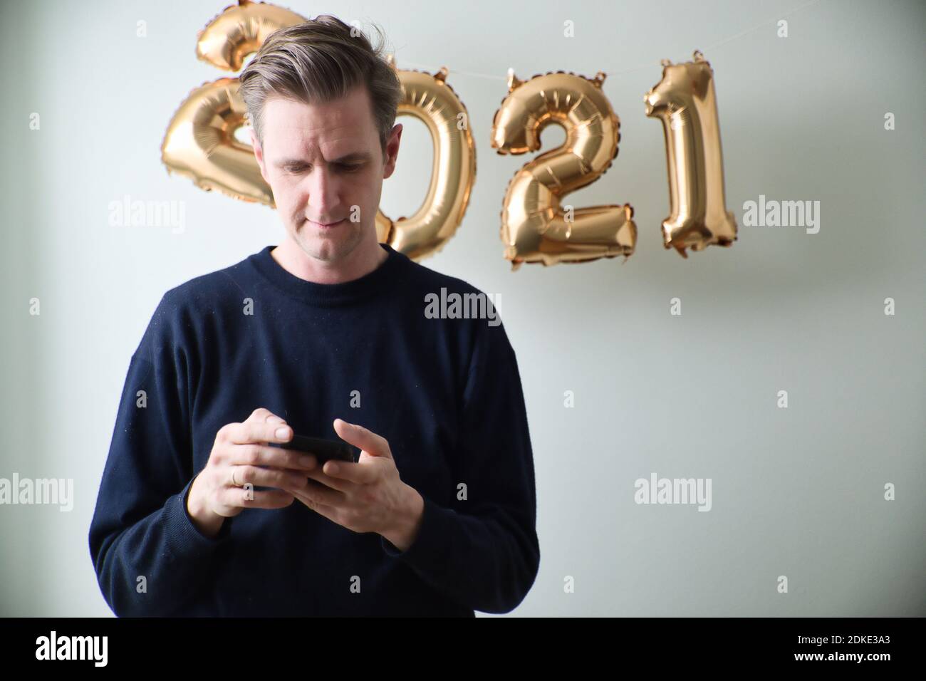 Caucasian man using phone in front of 2021 balloons indoor. Looking down. Medium shot. Stock Photo