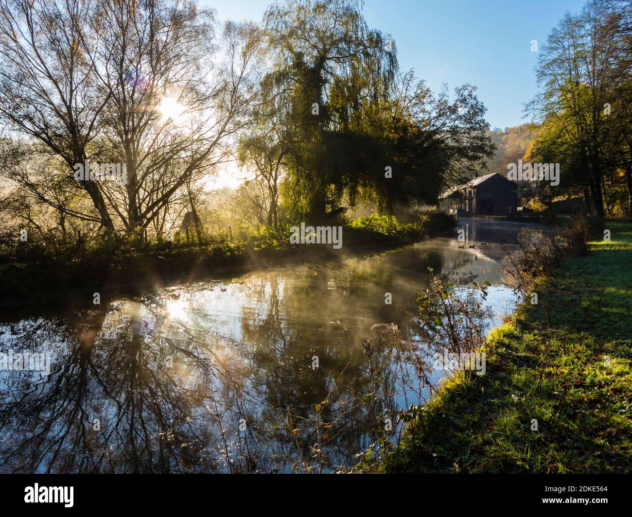 Early morning sunshine streaming through mist and trees on the Cromford Canal in the Derbyshire Peak District England UK Stock Photo