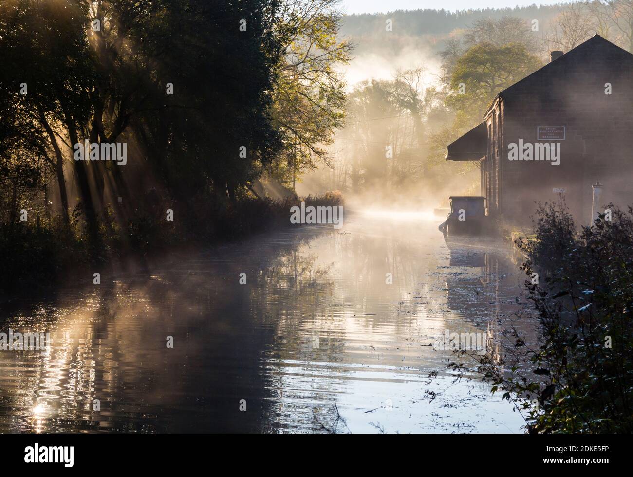 Early morning sunshine streaming through mist and trees on the Cromford Canal in the Derbyshire Peak District England UK Stock Photo