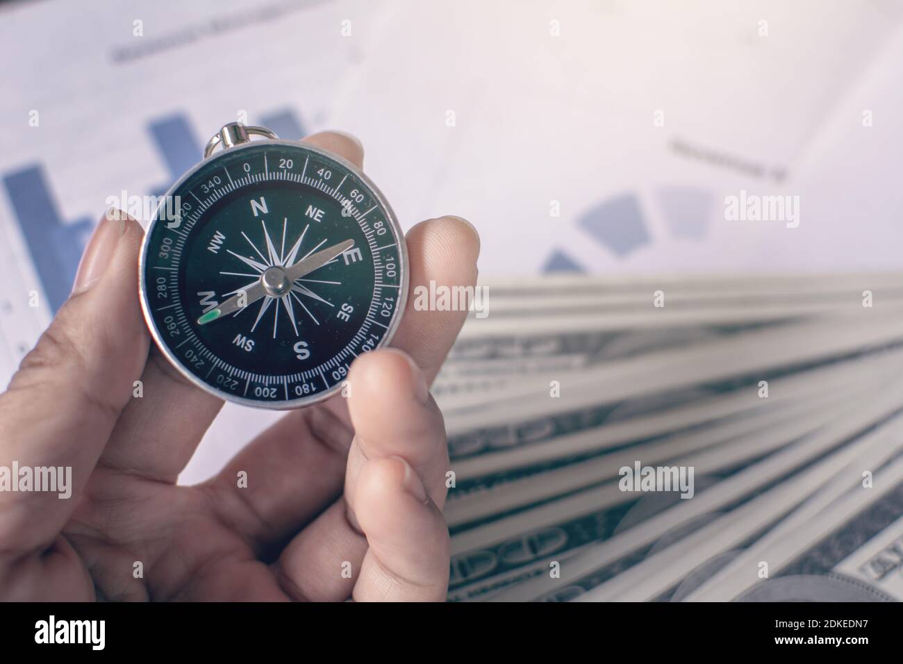 Cropped Hand Holding Navigational Compass Against Papers Stock Photo