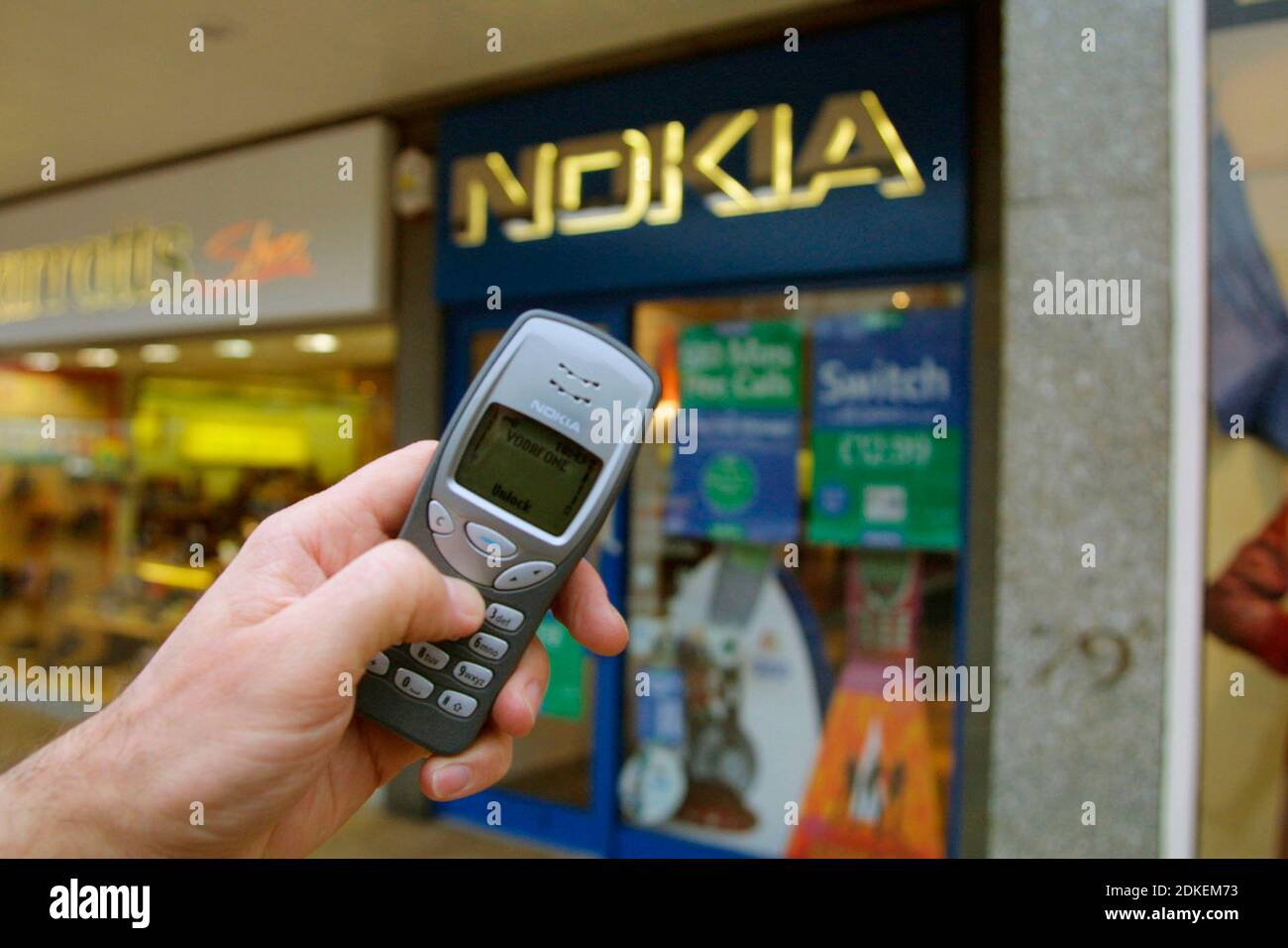 A hand holding a Nokia 3210 mobile phone in front of a Nokia shop, in Edinburgh, Scotland. This was a highly popular cellular phone released in 1999. Stock Photo