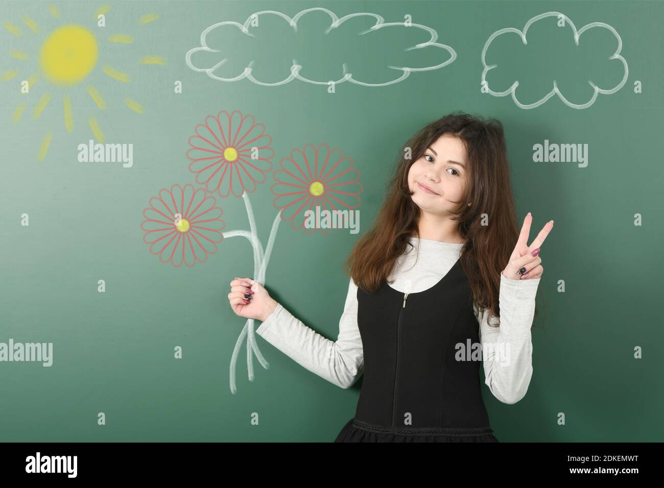 Portrait of a cheerful pretty pre-adolescent child holding painted flowers on background of school board. Looking at camera. High resolution photo. Fu Stock Photo