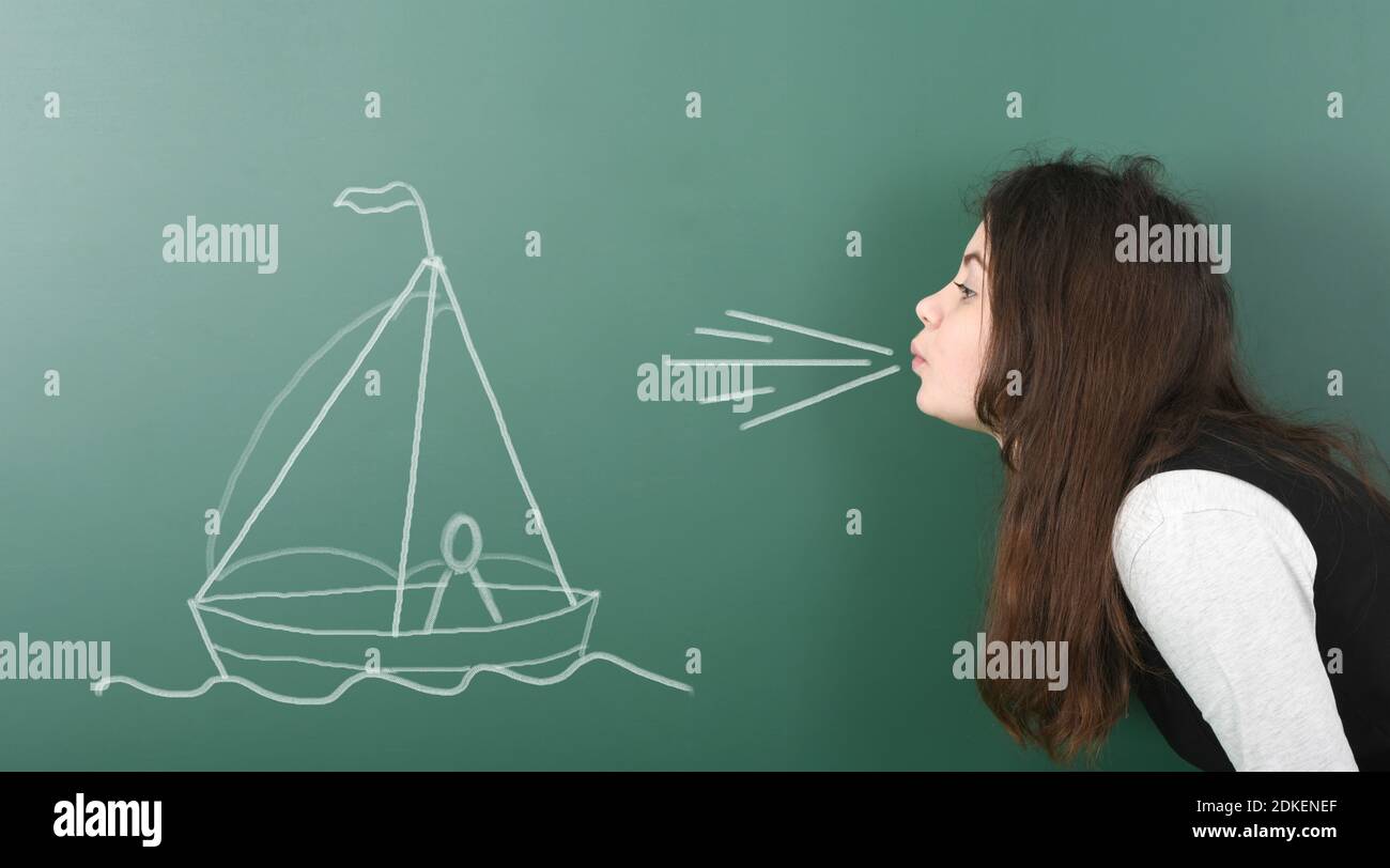 Pre-adolescent girl blowing on painted sailing ship. Portrait photo on school board background. High resolution photo. Full depth of field. Stock Photo
