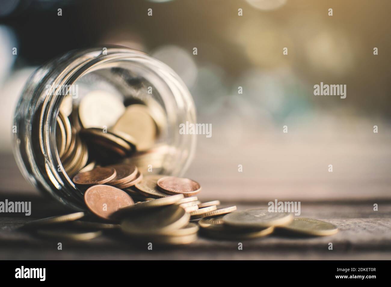Close-up Of Coins Falling From Glass Jar On Table Stock Photo