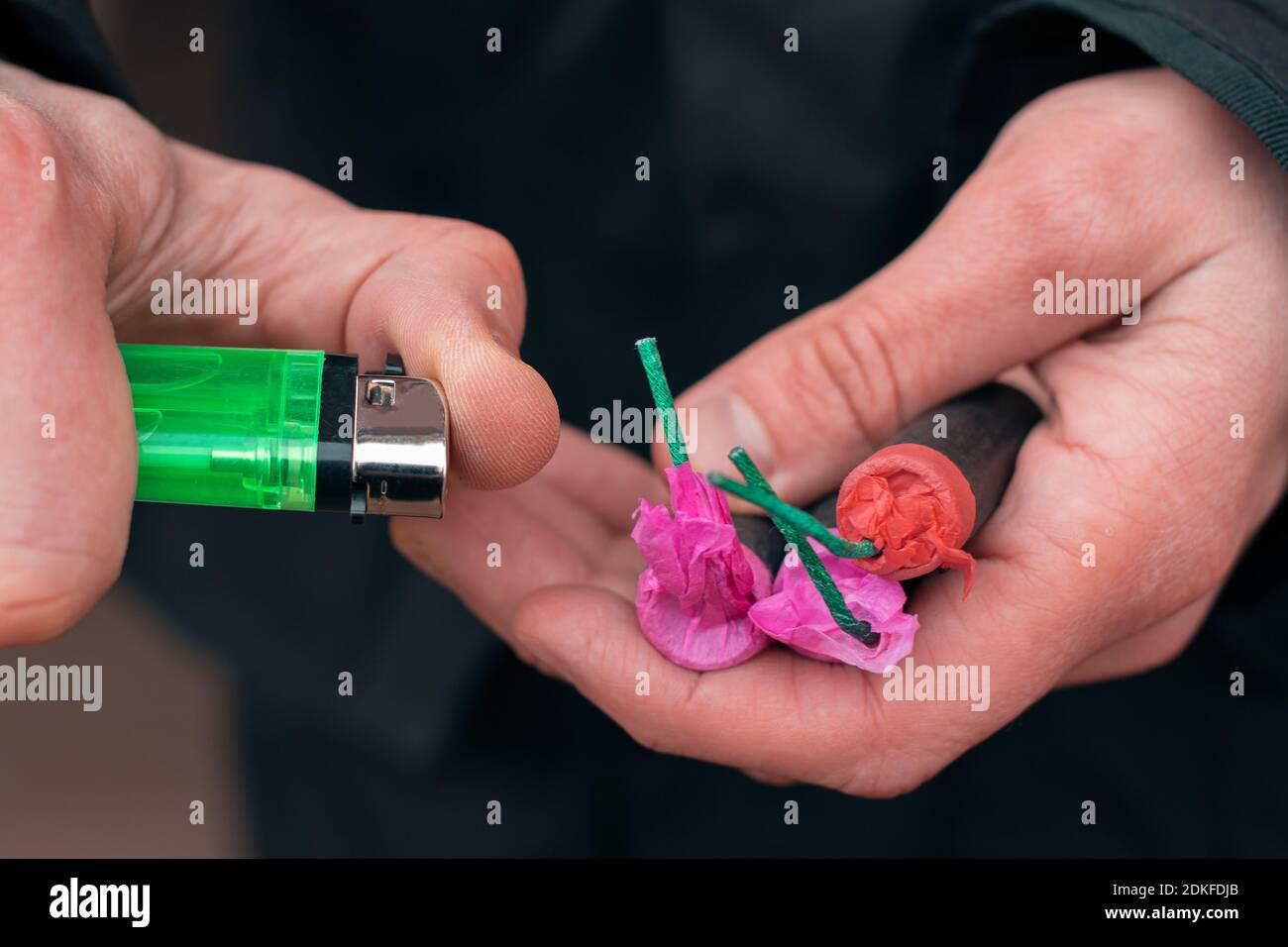 Setting Fire to the several Firecrackers. Man in Black Clothes Lighting Up Two Petards at the Same Time. Firing Up the Pyrotechnic with Green Gas Lighter Outdoors Stock Photo