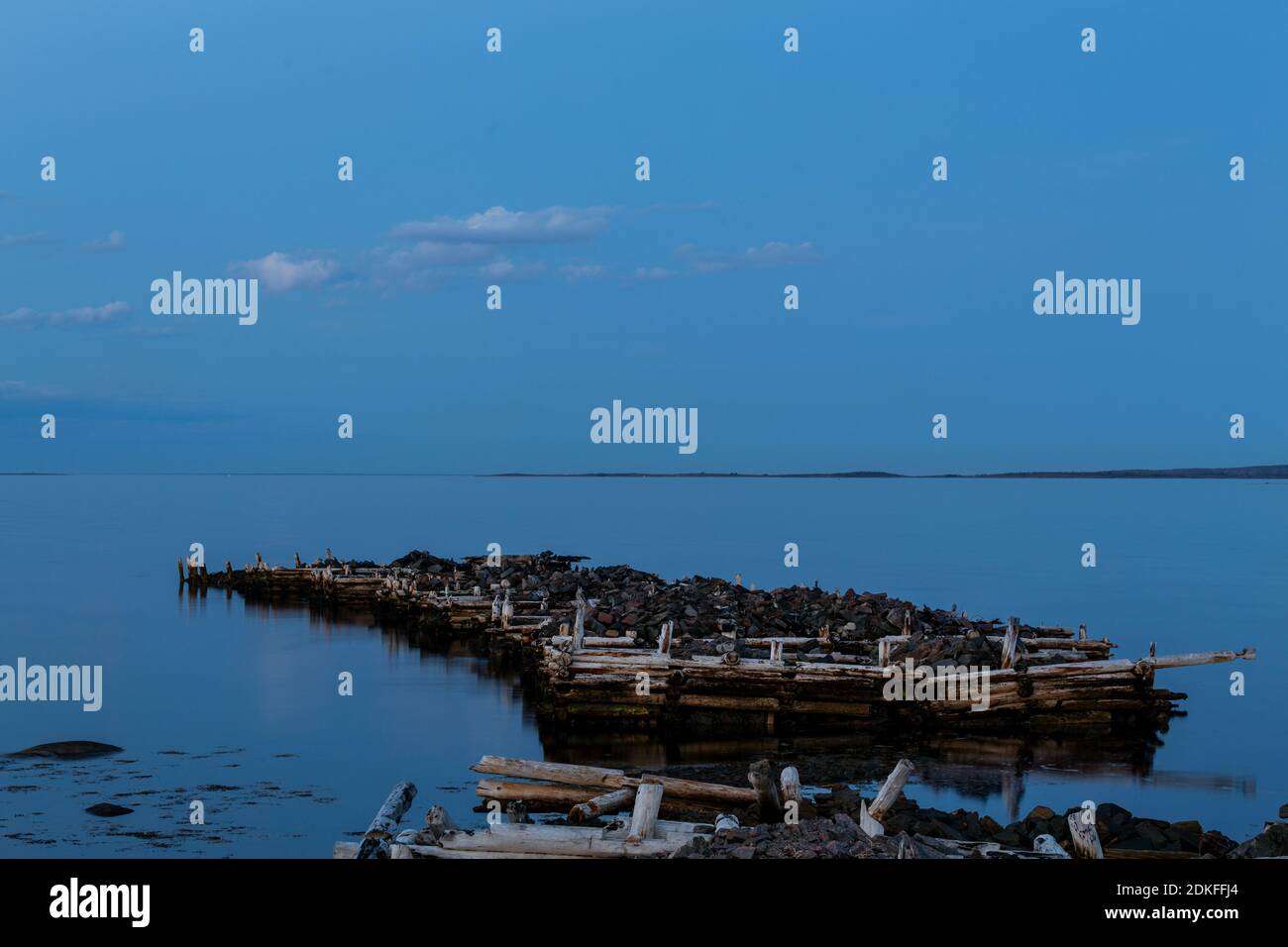 Old ruined pier in the sea on a cloudy, nasty full moon late evening, White Sea, Russia Stock Photo