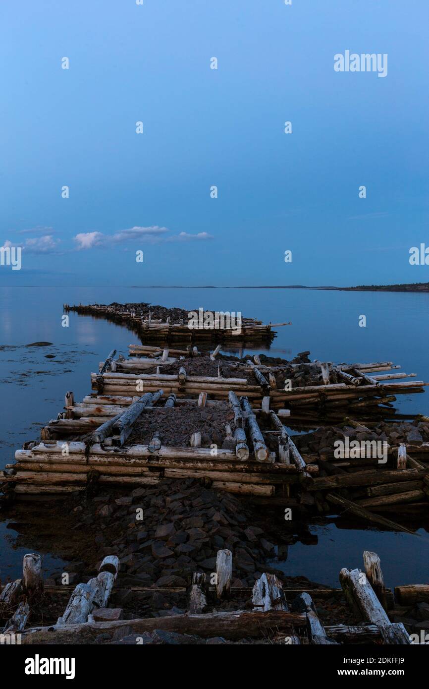 Old ruined pier in the sea on a cloudy, nasty full moon late evening, White Sea, Russia Stock Photo