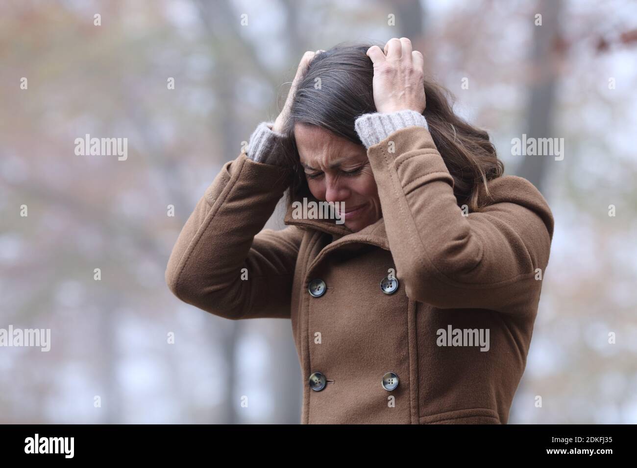 Desperate woman complaining alone grabbing hair with hands in a park in winter Stock Photo