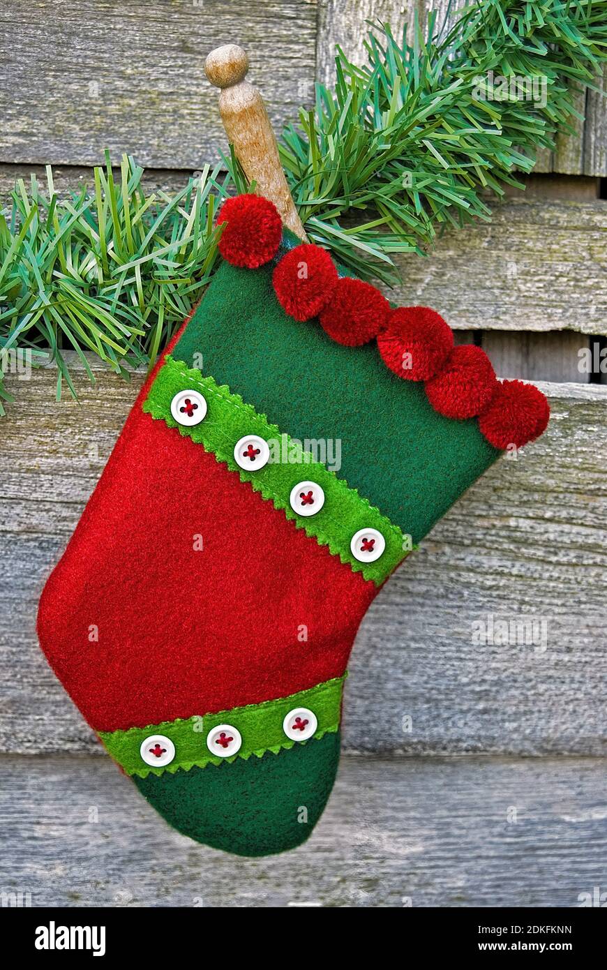 red and green Christmas stocking hanging from retro wooden clothespin and holiday pine garland on rustic barn wood Stock Photo