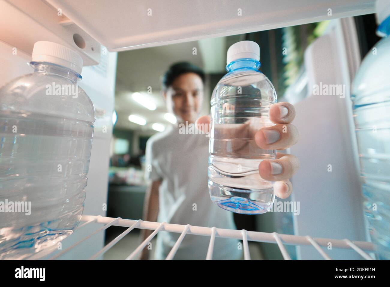 Asian man storing plastic bottles of drinking water in refrigerator