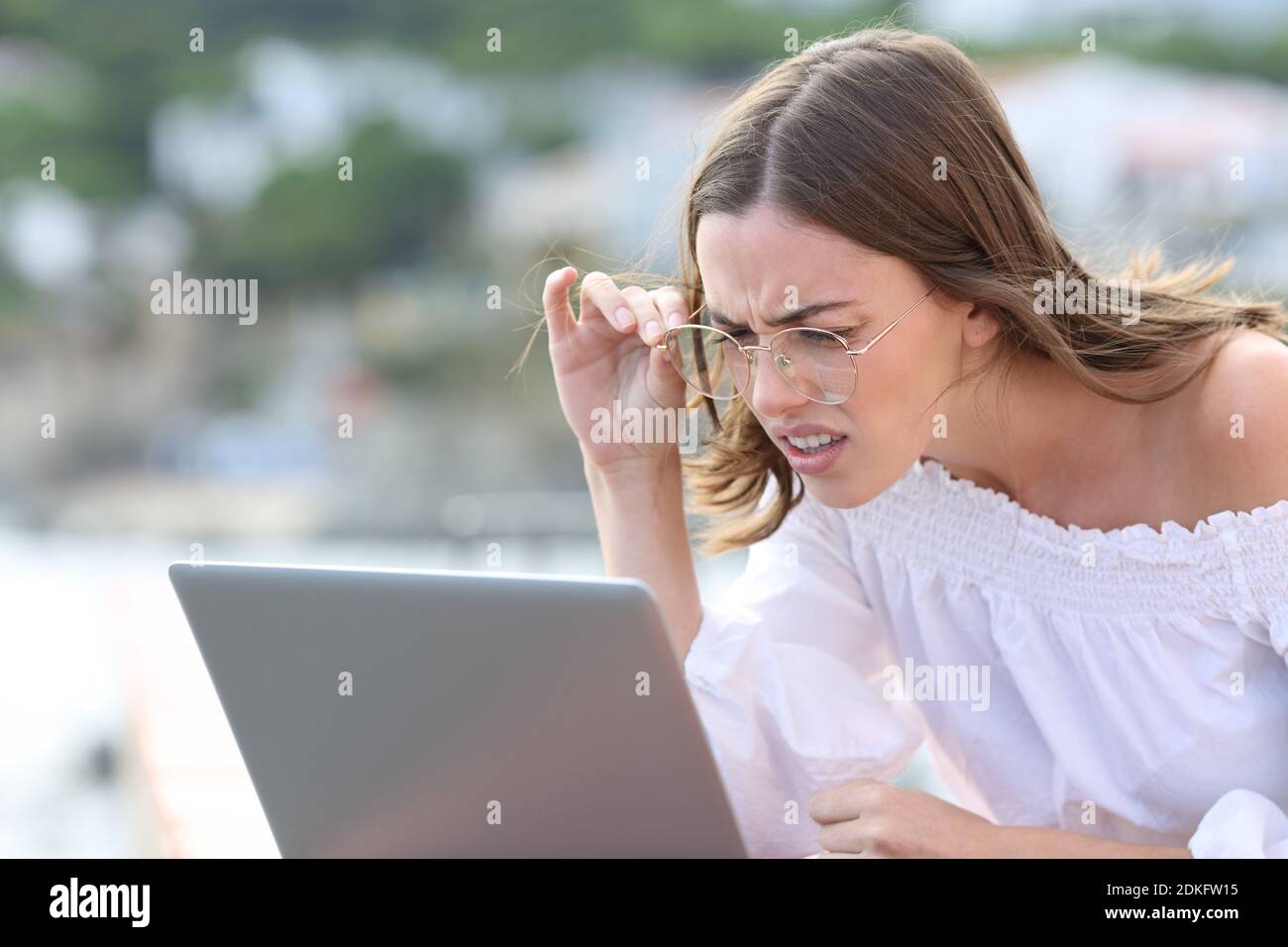 Stressed woman with eyeglasses forcing sight using laptop outdoors Stock Photo