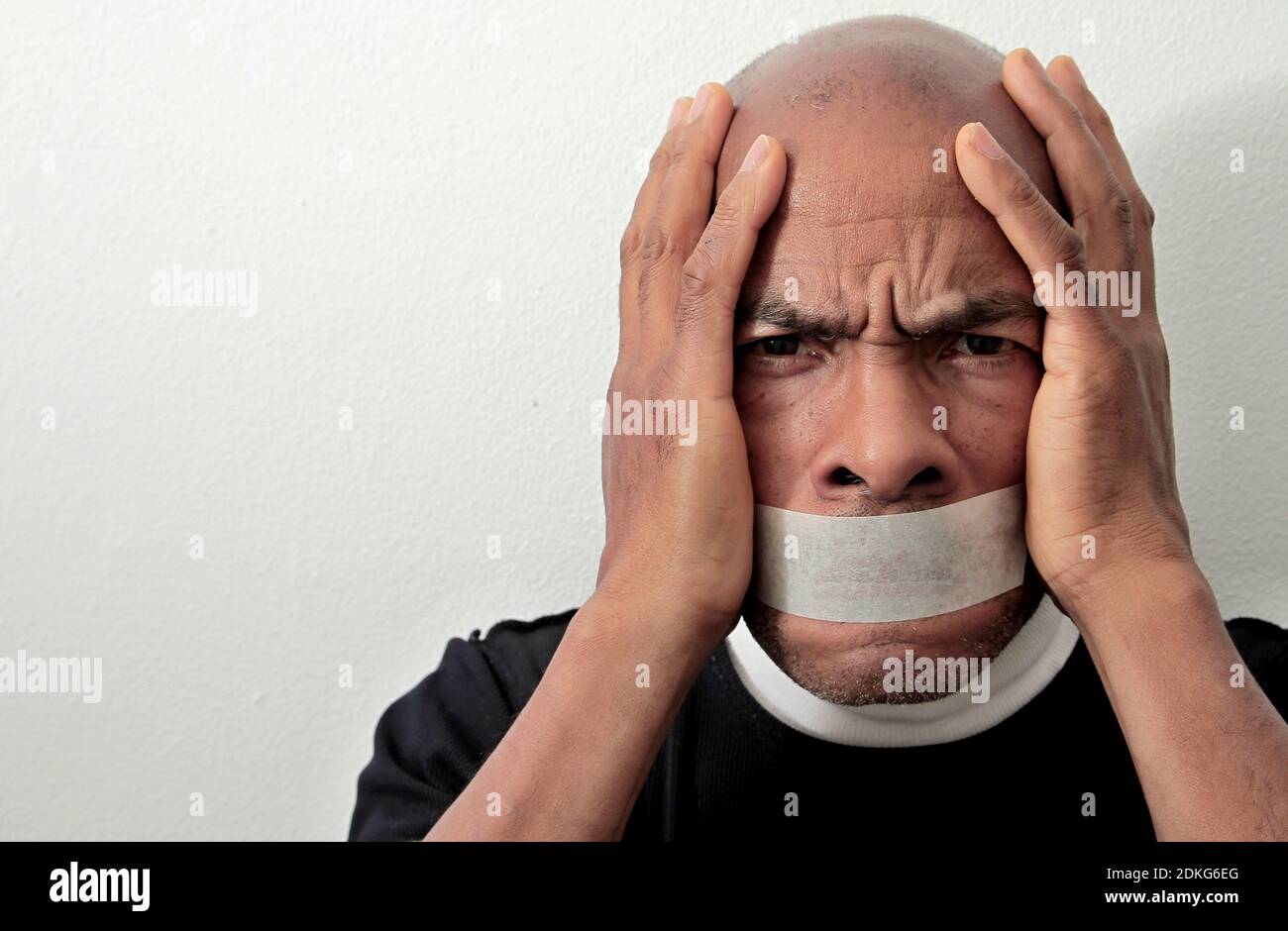 men feeling the pain after being discriminated with tape over his mouth on white background stock photo Stock Photo