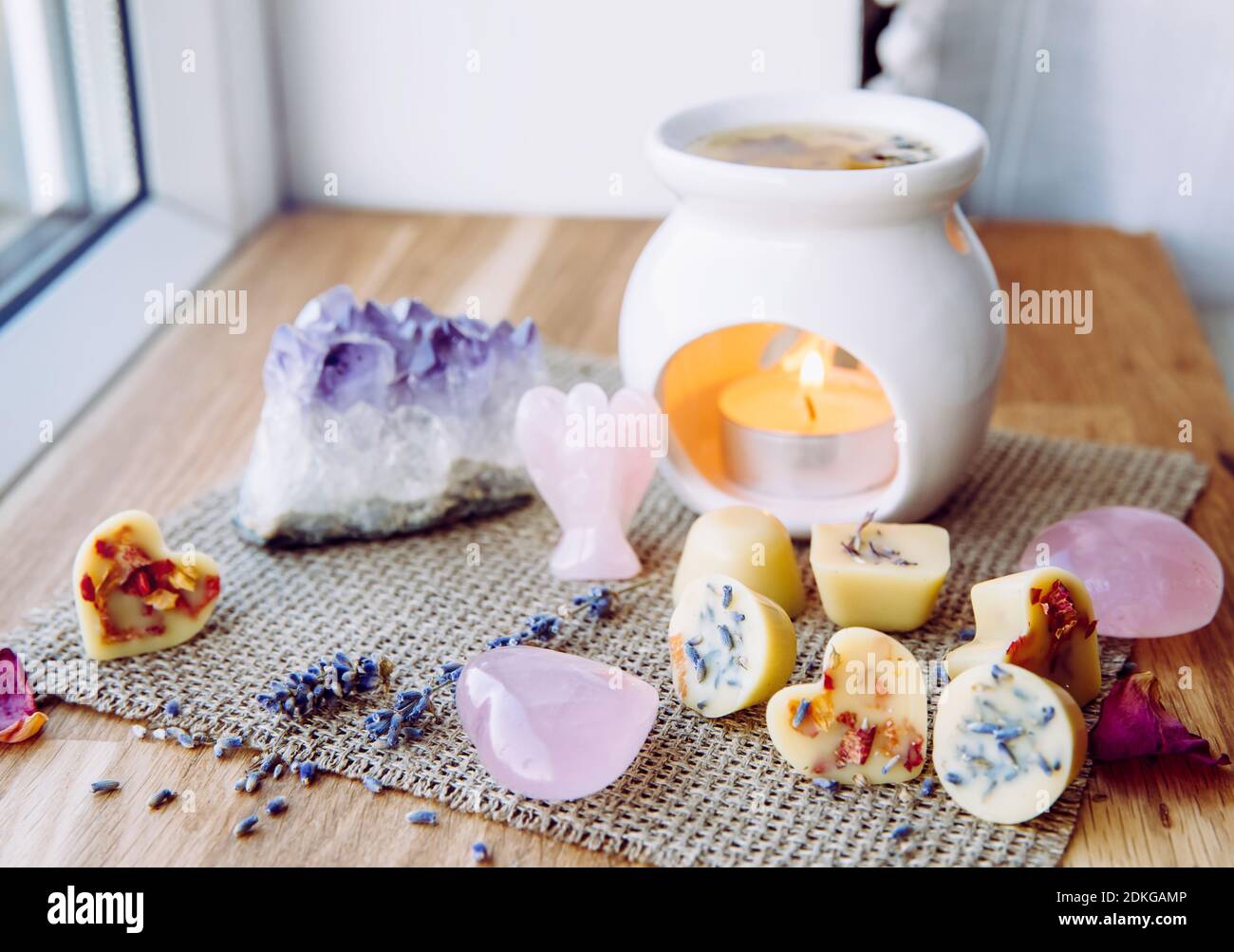 Homemade mini wax melts in aromatherapy lamp diffuser at home interior with rose quartz crystal hearts and angel for decoration on wooden window sill Stock Photo