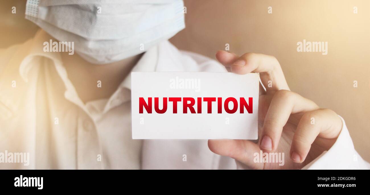 A doctor wearing face mask holds a card with the text NUTRITION . Medical concept. Stock Photo