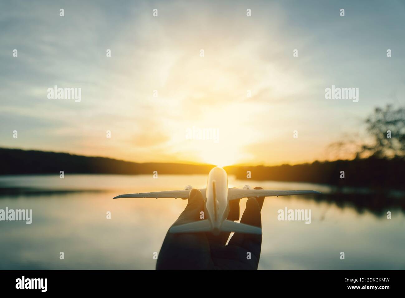Cropped Hand Of Person Holding Model Airplane By Lake Against Sky During Sunset Stock Photo