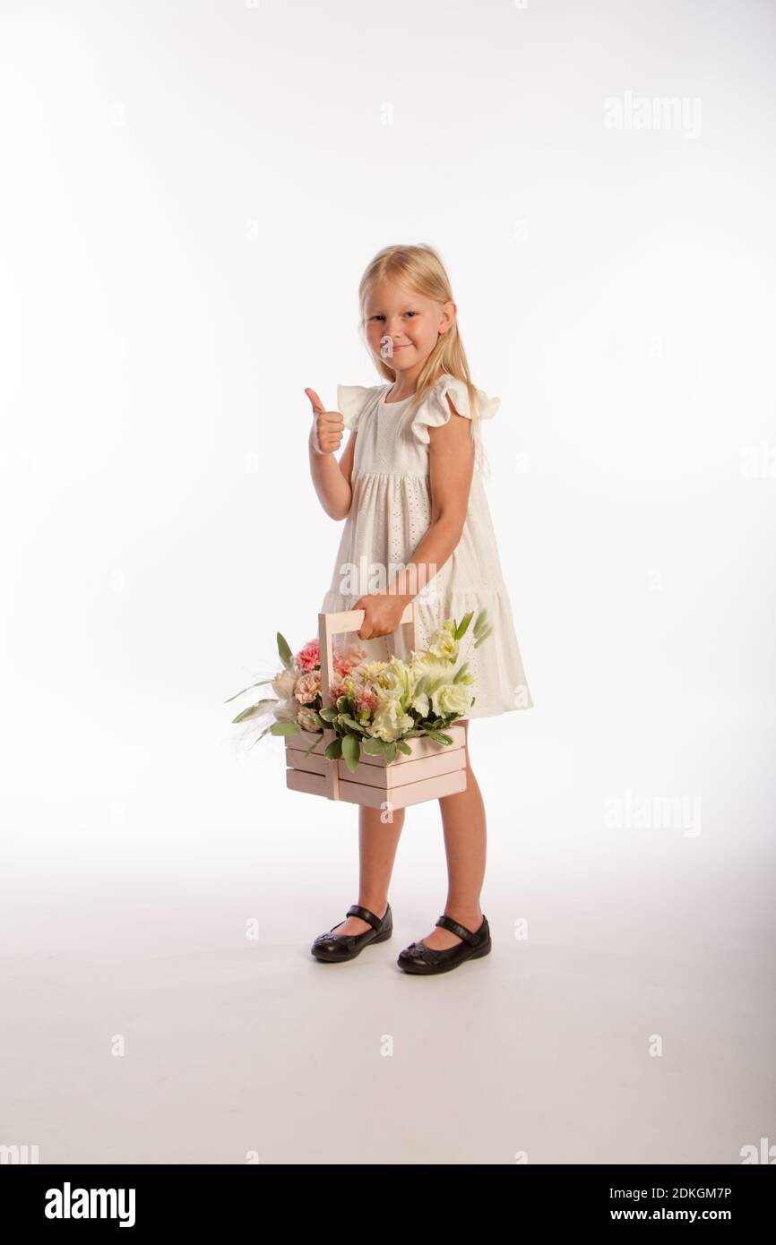 Studio portrait of cute blonde girl in white dress with wooden basket of flowers, white background, selective focus Stock Photo