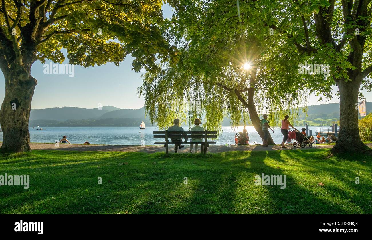 aged couple sitting on a bench under a tree and looking at sunset at Tegernsee, southern Bavaria. Stock Photo