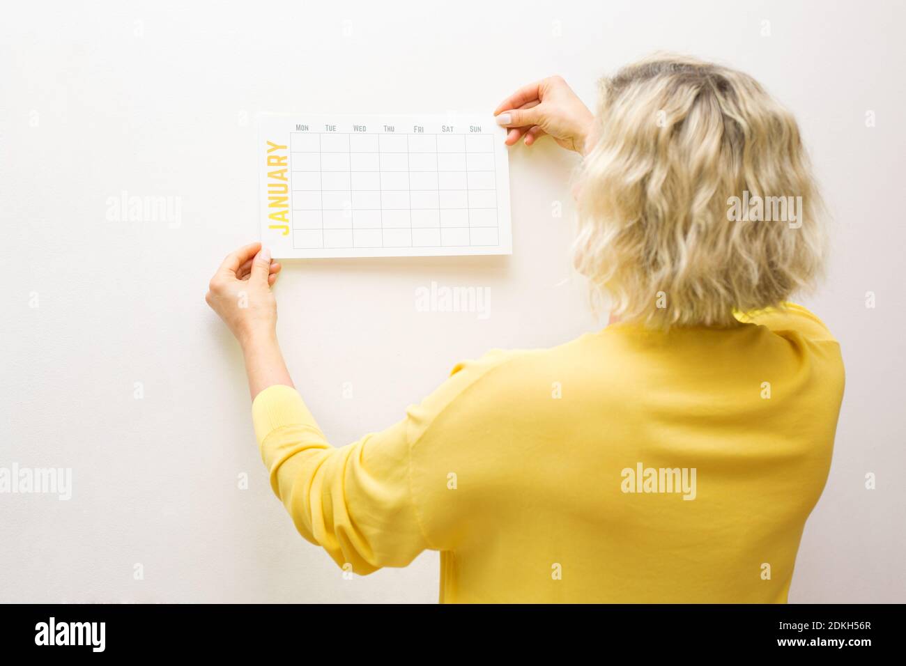 A woman's hand hangs up a new calendar for January.Goal, action, strategy, decision, business success concept.Minimal concept Stock Photo
