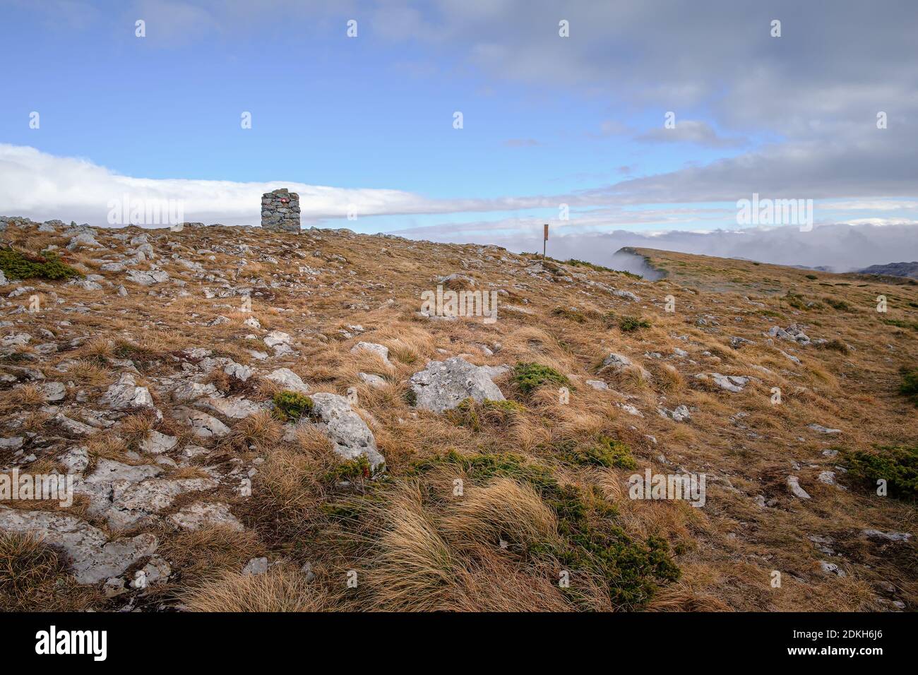 Autumn colored, dry grass on popular peak Trem on Dry mountain (Suva planina) with summit stone, background mist and cloudy, blue sky Stock Photo