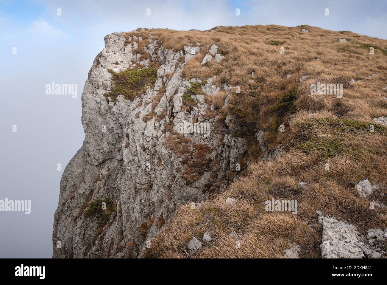 Rocky, steep, vertical cliff on Dry mountain (Suva planina) covered with dry, orange grass at autumn and cloudy blue sky Stock Photo