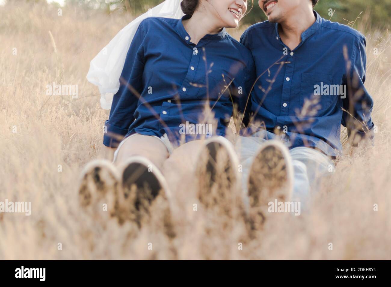Low Section Of Couple Sitting On Grassy Field Stock Photo