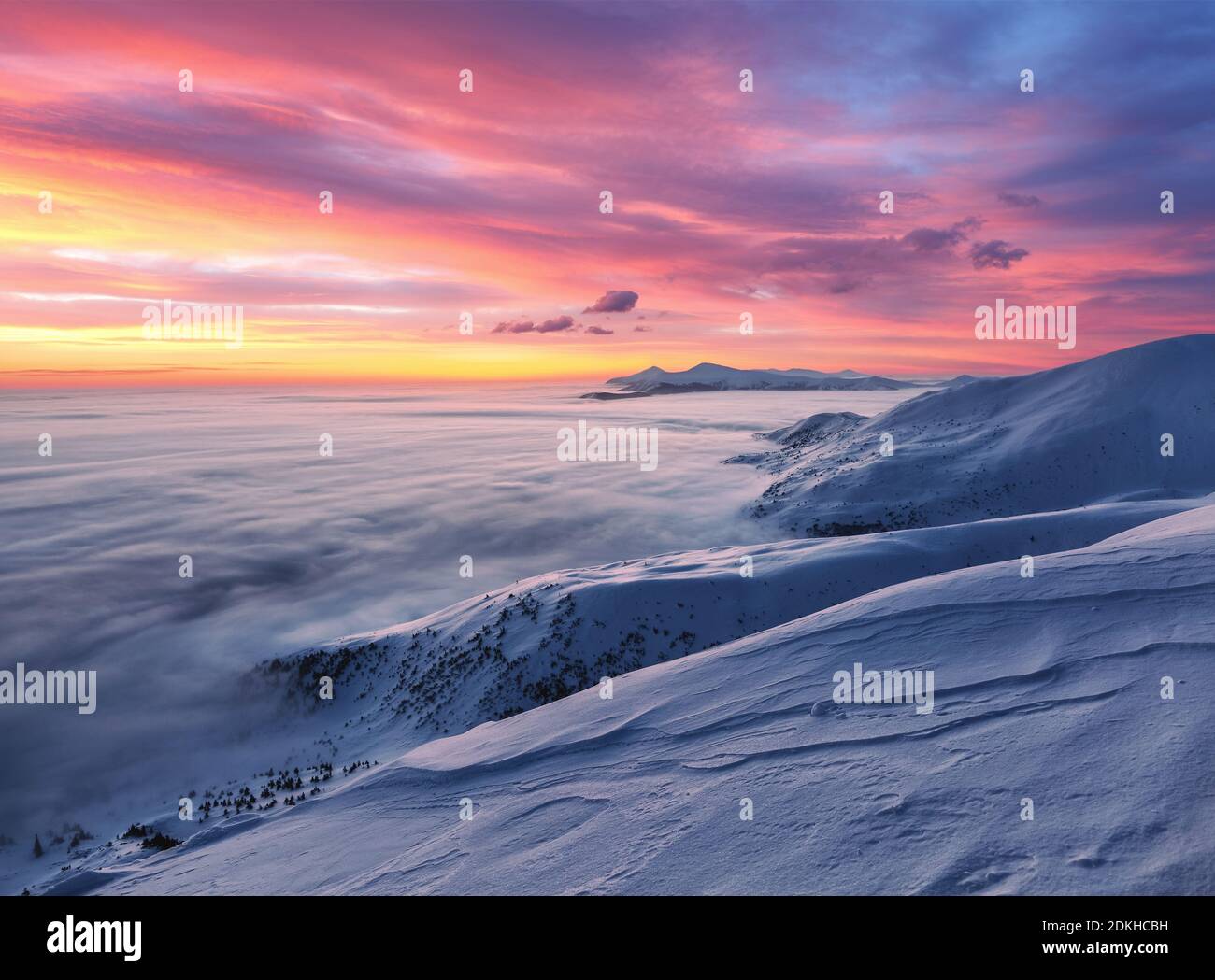 Majestic sky with pink cloud. Fantastic sunrise illuminates the mountain, thick fog and horizon. Snowy winter morning. Wallpaper background. Location Stock Photo