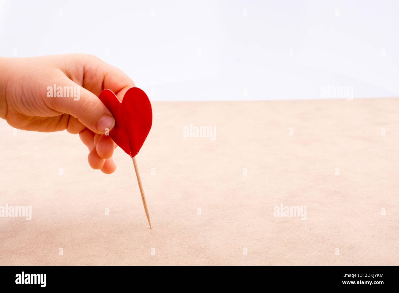 Closeup Of Hand Holding Red Heart Shape With Toothpick On Table