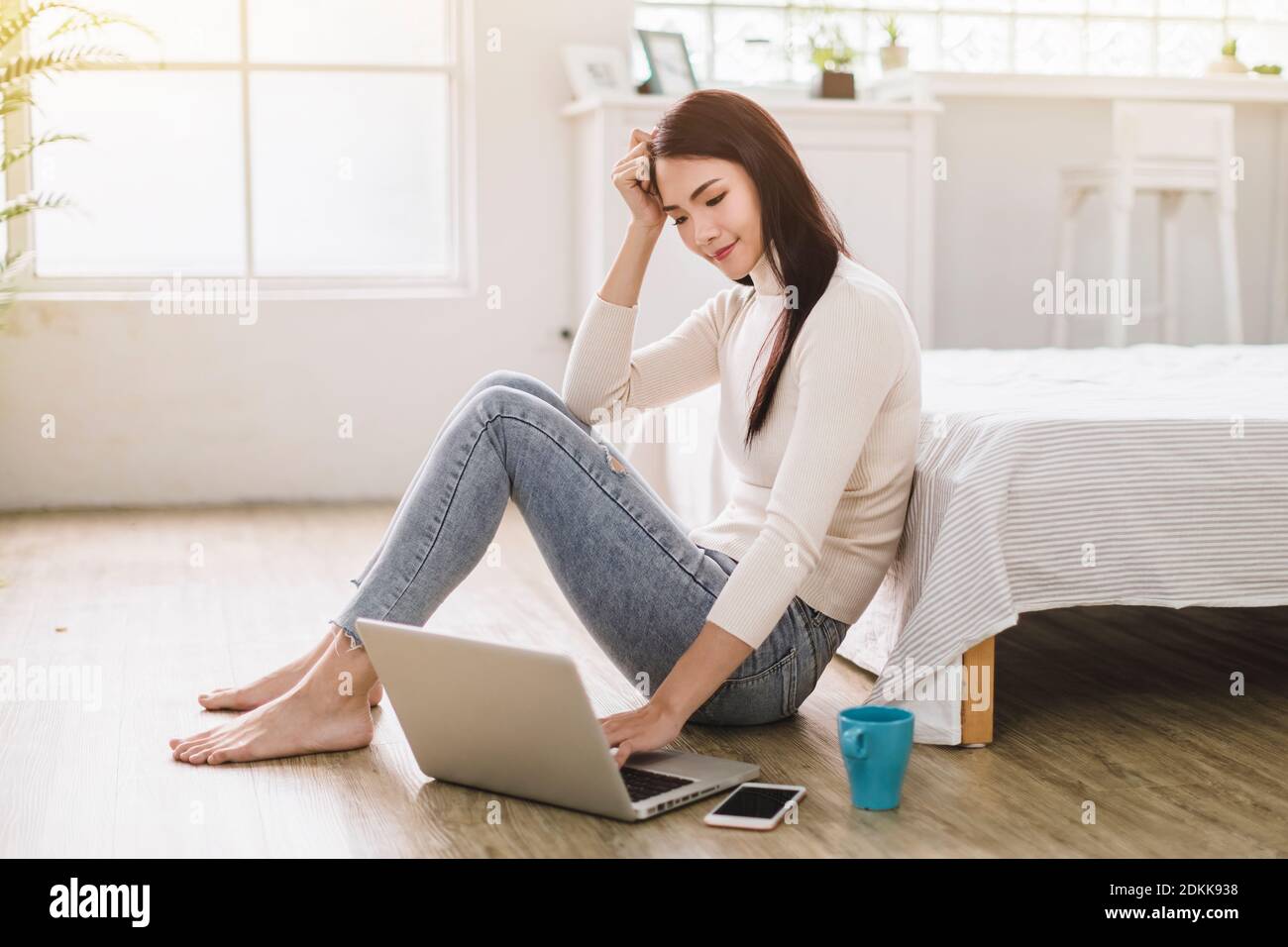 Beautiful young smiling woman working on laptop and drinking coffee at home Stock Photo