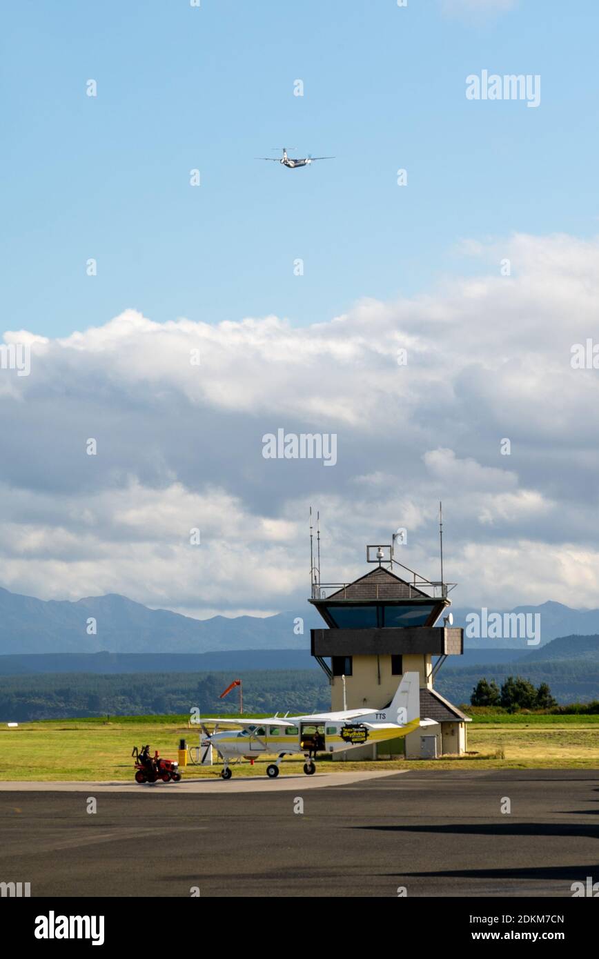 A Bombardier Dash 8 Q300 series departs in the distance, a disused control tower and a Cessna C208 Caravan in the foreground. Taupo Airport, NZ Stock Photo