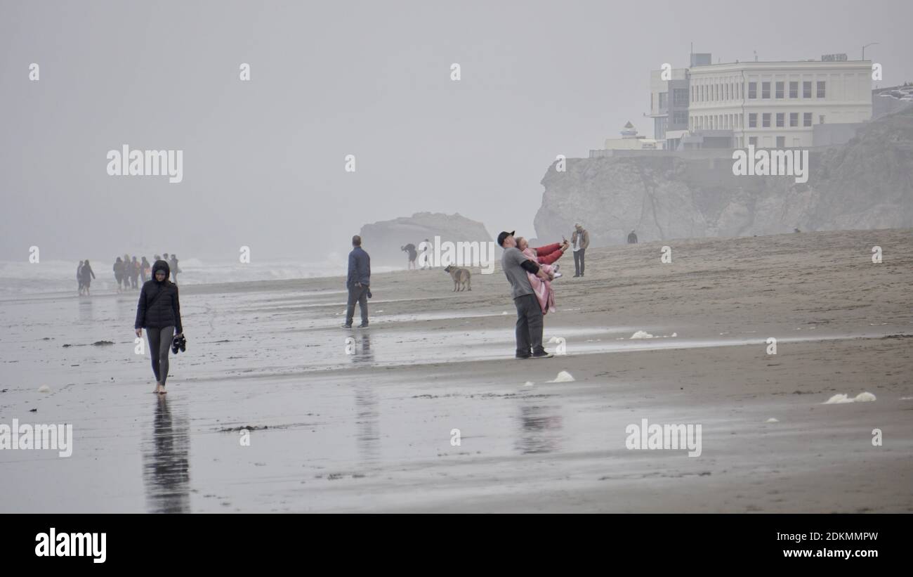 Beach walkers visiting Ocean Beach on a very foggy day with The Cliff House in the background. San Francisco, California Stock Photo
