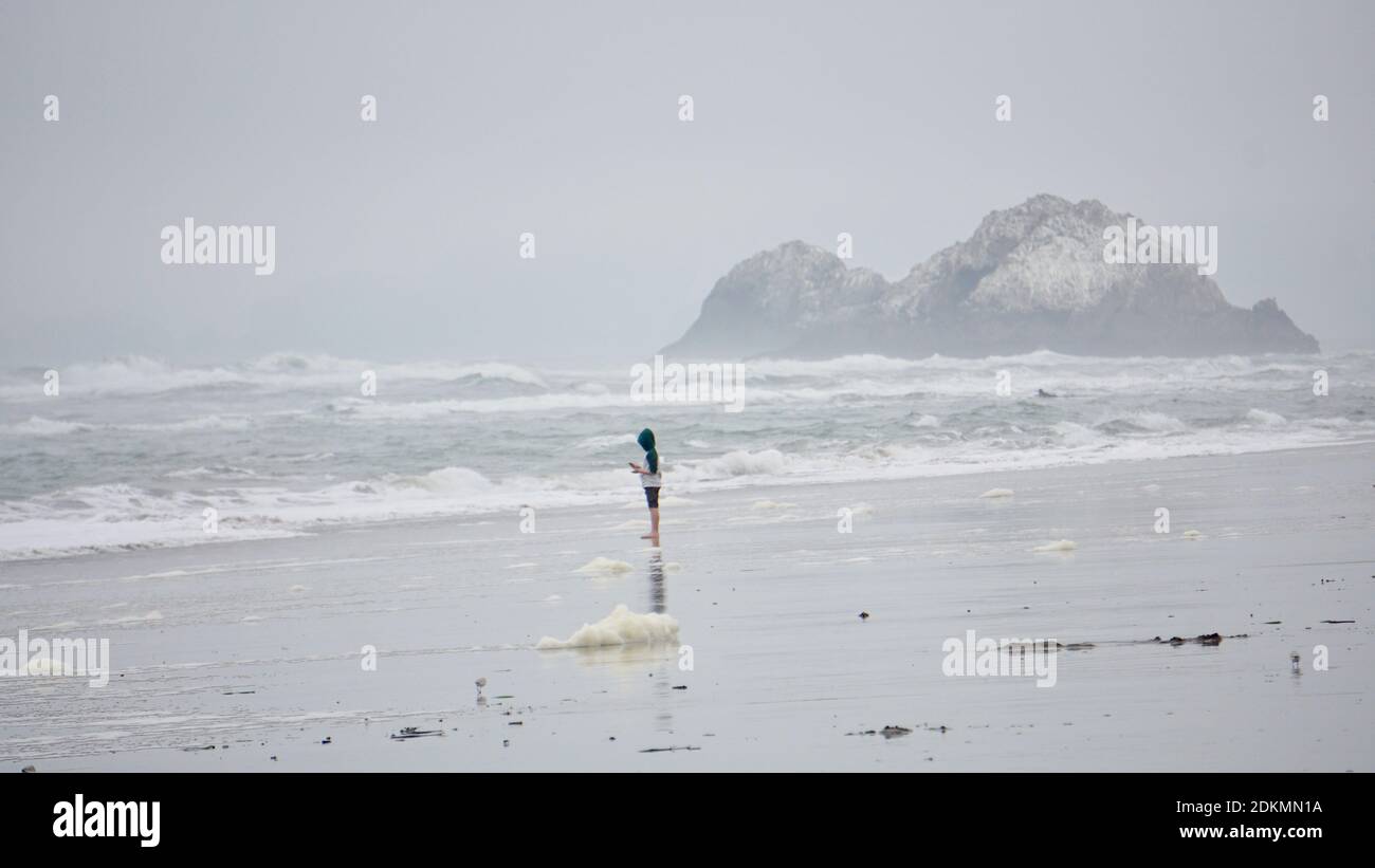 Child barefoot on Ocean Beach on a very foggy day, with The Seal Rocks in the background, near the Cliff House. San Francisco, California, USA Stock Photo