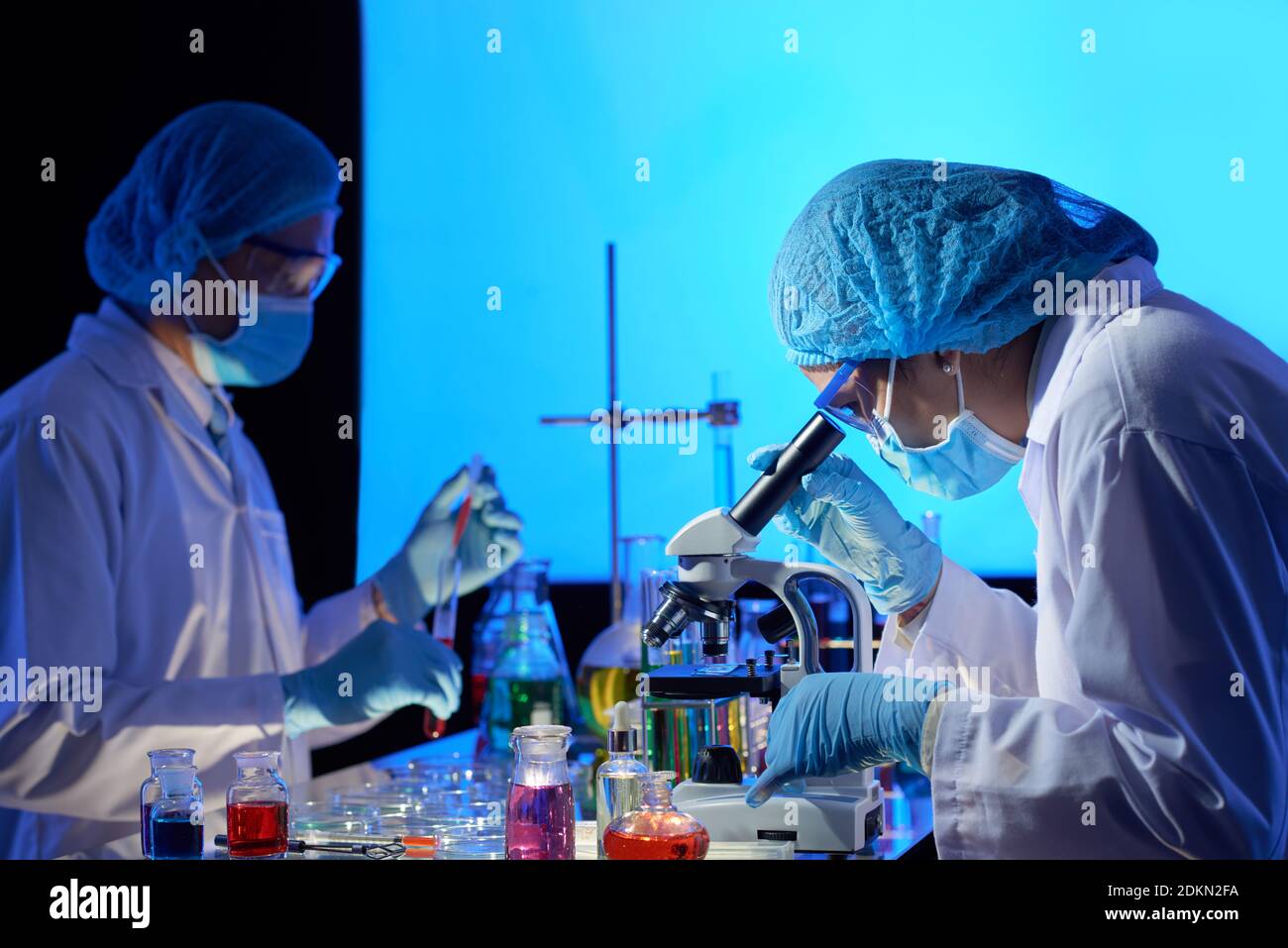 Team of scientists working on covid-19 vaccine in dark laboratory, mixing liquids and looking through microscope Stock Photo