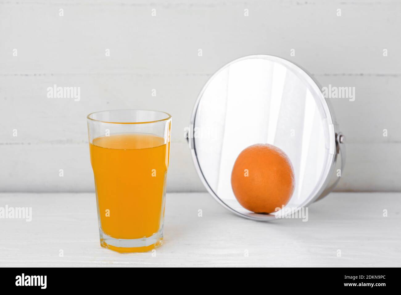 Glass of orange juice looking at its reflection in mirror on white wooden background Stock Photo