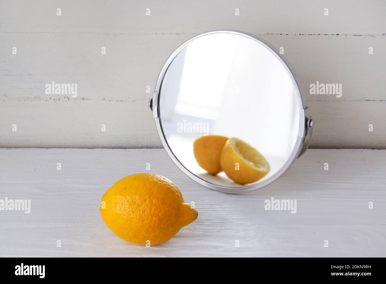 Lemon looking at its reflection in mirror on white wooden background Stock Photo
