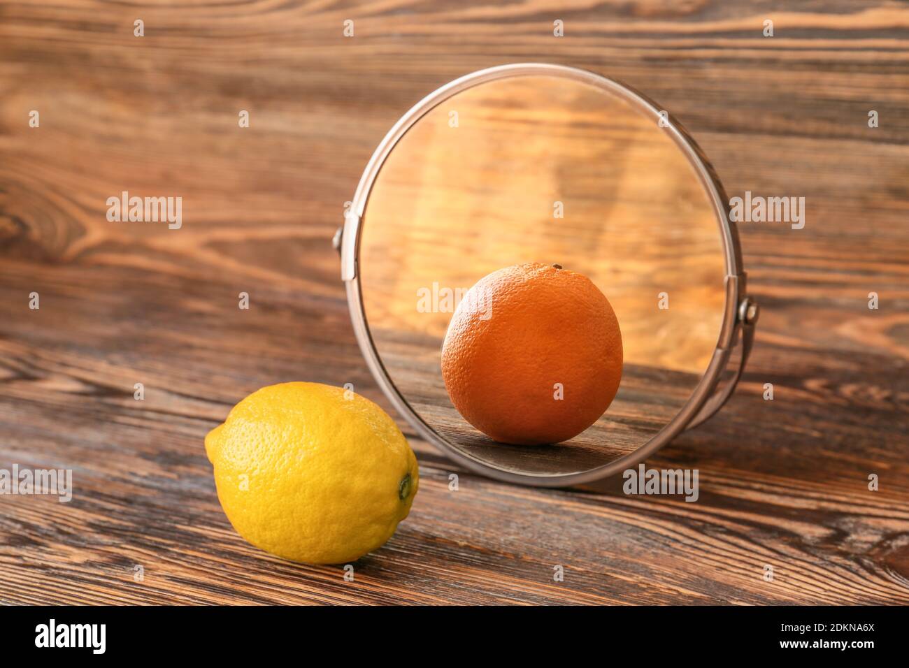 Lemon looking at its reflection in mirror on wooden background Stock Photo