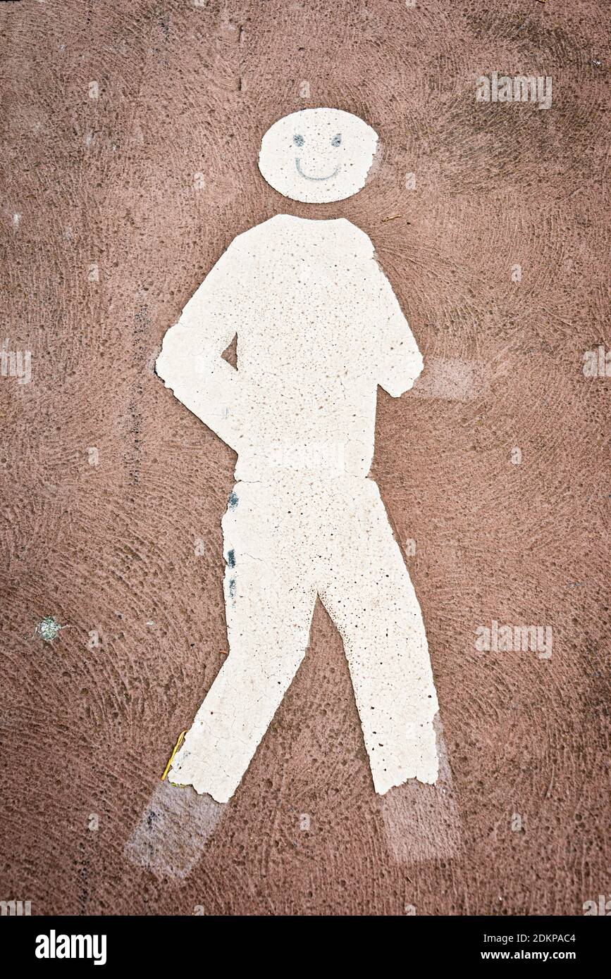 an old, weathered and fading pedestrian symbol with parts of the symbol being broken away, and a smiley face drawn upon it, vertical Stock Photo