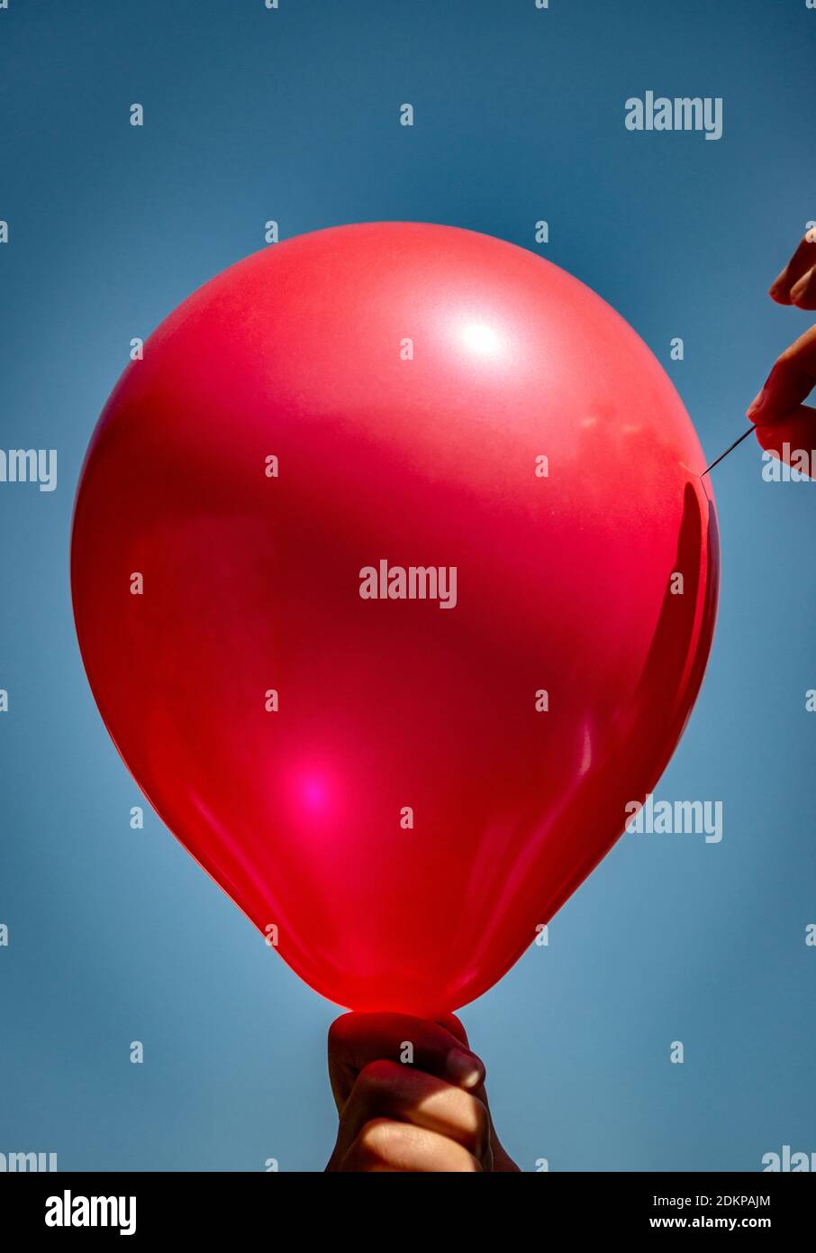 hands holding a red balloon and a pin threatening to pop it, needle against  the balloon, against a bright blue sky Stock Photo - Alamy