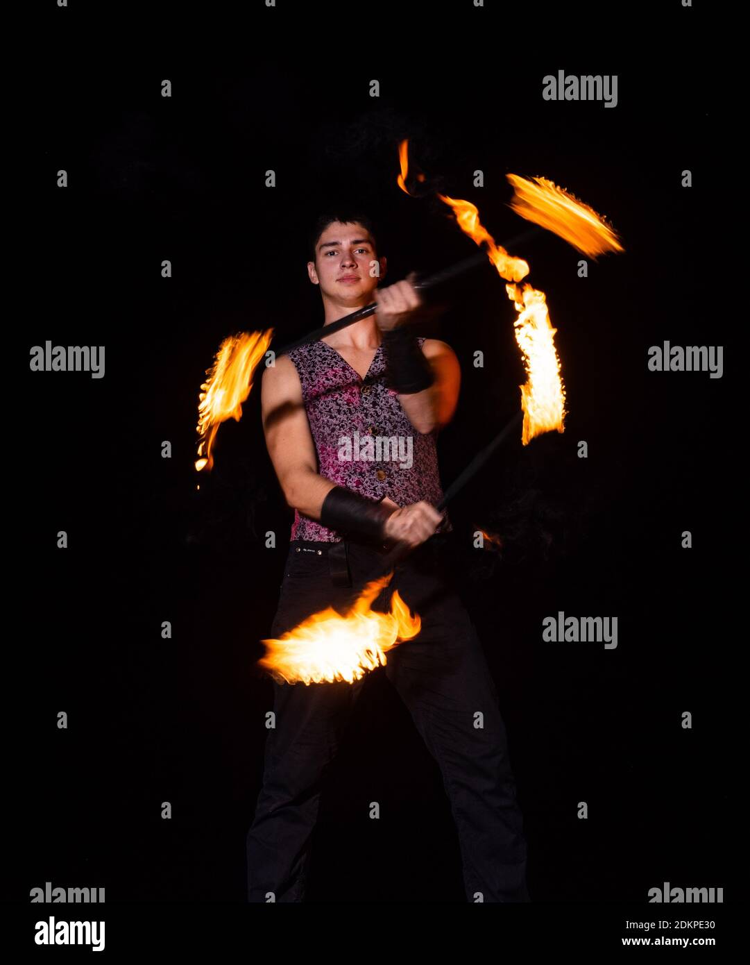 Burning energy. Handsome man juggle flaming batons. Fire juggling. Fire energy. Energetic twirling. Flame and sparks. Night performance. Amusement show. Light up and juggle. Stock Photo